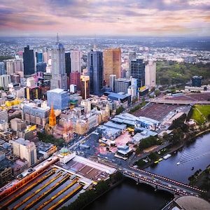 Puede incluir: Una vista aérea de un horizonte urbano al atardecer. La ciudad está llena de edificios altos, y un río atraviesa el centro de la imagen. Hay muchos árboles y parques en la ciudad, y el cielo es una hermosa mezcla de rosa, naranja y morado.