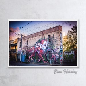 Puede incluir: Un mural colorido en el lateral de un edificio representa una criatura roja similar a un pulpo con una cara humana. El mural est&aacute; situado en el fondo de una calle de la ciudad con l&iacute;neas el&eacute;ctricas y &aacute;rboles. El texto del mural dice "Spread the love, share what you know and be the change you want to see in the world."