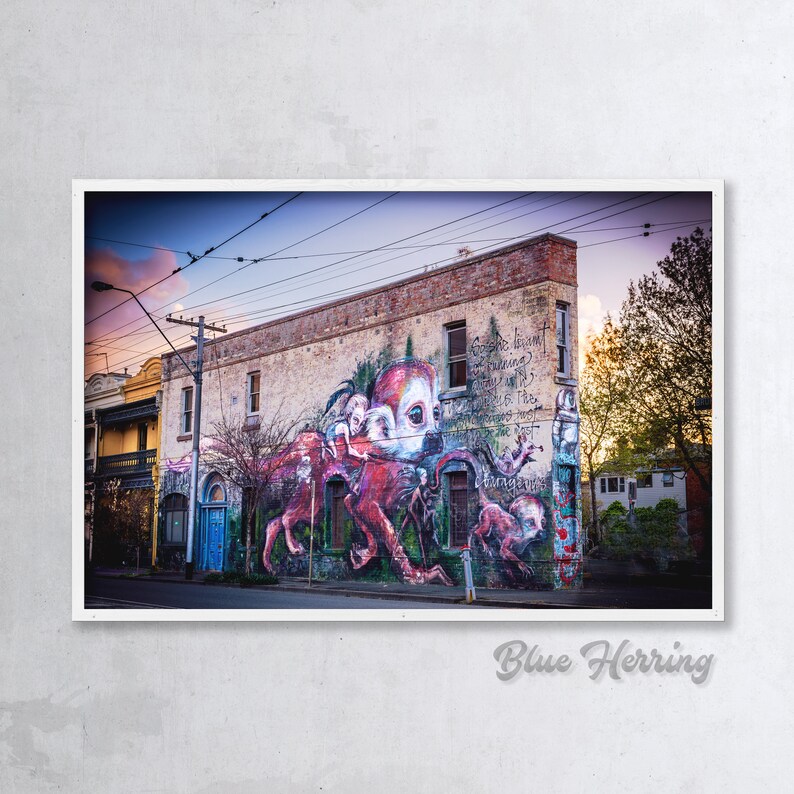 Puede incluir: Un mural colorido en el lateral de un edificio representa una criatura roja similar a un pulpo con una cara humana. El mural est&aacute; situado en el fondo de una calle de la ciudad con l&iacute;neas el&eacute;ctricas y &aacute;rboles. El texto del mural dice "Spread the love, share what you know and be the change you want to see in the world."