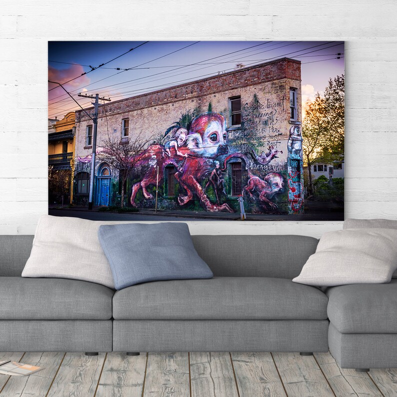 Puede incluir: Un mural colorido pintado en el lateral de un edificio de ladrillo. El mural representa una gran criatura roja similar a un pulpo con m&uacute;ltiples brazos y ojos. La criatura est&aacute; rodeada de figuras m&aacute;s peque&ntilde;as y texto que dice "El sue&ntilde;o permanece...", "...y el fuego", "...nos cambia".