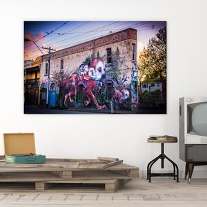 Puede incluir: Un mural de arte callejero colorido que representa una criatura multicolor similar a un pulpo con tent&aacute;culos en un edificio de ladrillo. El mural est&aacute; pintado en el lateral de un edificio con una puerta azul y ventanas. El edificio est&aacute; situado en una calle con l&iacute;neas el&eacute;ctricas por encima.