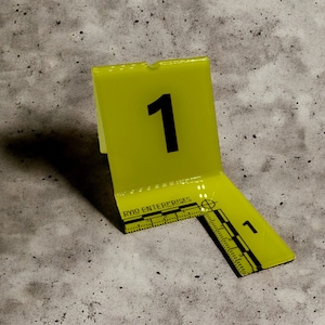 May include: Yellow crime scene marker with the number "1" printed on it. The marker is made of a flexible plastic material and has a ruler on the bottom.