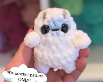 May include: A white crocheted plush toy with blue details and large black eyes. The toy is being held in a hand. PDF crochet pattern ONLY! is written on a blue cloud.