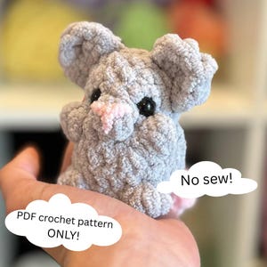 Op de afbeelding: Een grijze gehaakte muis met een roze neus en zwarte ogen. De muis wordt in een hand gehouden. De tekst "Geen naaiwerk!" en "PDF haakpatroon ALLEEN!" staat in de afbeelding.