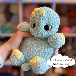 May include: A handmade, light blue crochet turtle plushie with yellow accents on its flippers and head. The turtle has large, sparkly eyes and is made with a soft, textured yarn. The text "Pdf Pattern Only! No/Low Sew" is visible.