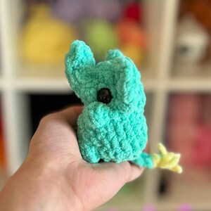 May include: A small, crocheted turquoise elephant toy with a yellow tail. The elephant has a black button eye.