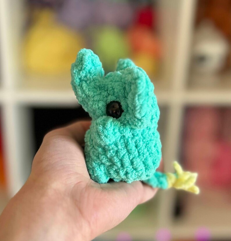 May include: A small, crocheted turquoise elephant toy with a yellow tail. The elephant has a black button eye.