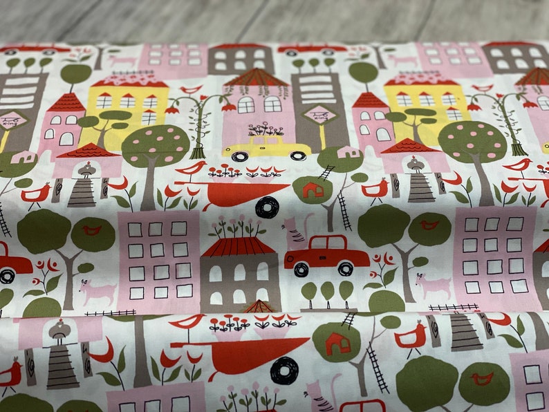 May include: White fabric with a repeating pattern of colorful houses, trees, cars, and birds. The houses are pink, yellow, and gray with red roofs. The trees are green with brown trunks. The cars are red and yellow. The birds are red, yellow, and blue.