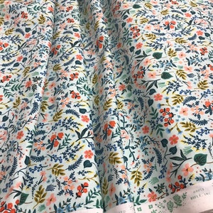 Peut inclure: Un rouleau de tissu avec un motif floral de la collection Wildwood. Le motif pr&eacute;sente de petites fleurs orange, roses et bleues, ainsi que du feuillage vert et dor&eacute;, sur un fond bleu clair. Le tissu est s&eacute;rigraphi&eacute; au Japon.