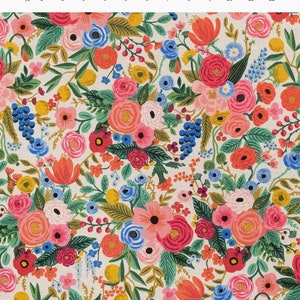 May include: A cream-colored fabric with a floral pattern. The pattern features pink, red, orange, yellow, blue, and green flowers. The flowers are arranged in a random pattern and are surrounded by green leaves.