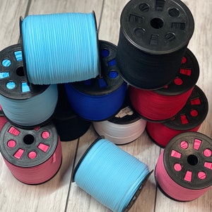 May include: Assortment of spools of colorful elastic cord, wound on black plastic bobbins. The cords are in shades of blue, pink, and white.