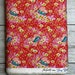 May include: Red fabric with a repeating pattern of pink and yellow flowers, green birds, and small butterflies. The fabric has a white border and a label that reads 'Free Spirit Presents Tiny Beasts'.