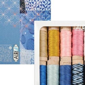 May include: A set of 12 spools of Aurifil thread in a white box. The thread colors are a mix of blues, pinks, yellows, and browns. The box has the Aurifil logo and the words "Breezy Moments" on it.