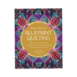 May include: A book cover for "Anna Maria's Blueprint Quilting." The cover features a colorful patchwork design in shades of purple, blue, and green. A gold circle in the center displays the book's title and author's name.