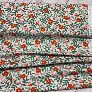 K&ouml;nnte beinhalten: Ein wei&szlig;er Stoff mit einem sich wiederholenden Muster aus roten und rosa Bl&uuml;ten, gr&uuml;nen Bl&auml;ttern und kleinen Schmetterlingen. Der Stoff hat einen wei&szlig;en Spitzenbesatz am Rand.