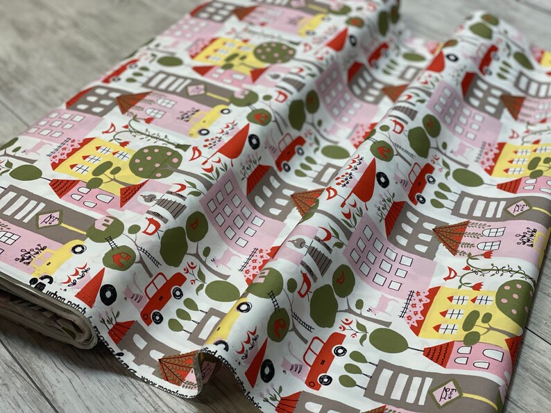 May include: White cotton fabric with a repeating pattern of colorful houses, trees, cars, and birds. The houses are pink, yellow, and gray with red roofs. The trees are green and the cars are red and yellow.