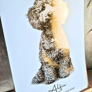 May include: A gold foil print of a dog named Alfie, sitting upright. The dog has fluffy fur and is set against a white background. The text reads "Alfie, You left your paw prints in my heart 2009-2026".