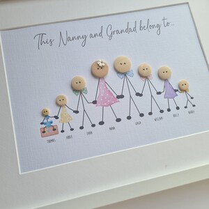 May include: A framed artwork with the text "This Nanny and Grandad belong to..." and a family of button people with names written below each figure. The family includes a grandmother, grandfather, and seven children.