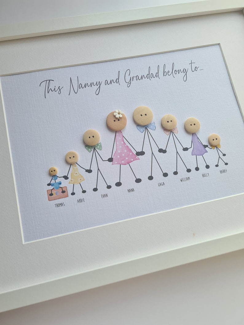 May include: A framed artwork with the text "This Nanny and Grandad belong to..." and a family of button people with names written below each figure. The family includes a grandmother, grandfather, and seven children.