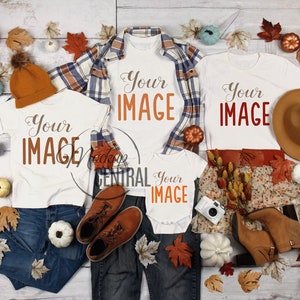 以下が含まれることがあります： 「Your IMAGE」の文字が入った白いTシャツ、ジーンズ、チェック柄のシャツ、オレンジ色のニット帽、茶色のフェドラハット、ブーツ、装飾用のカボチャと葉が配置された秋をテーマにしたフラットレイ。ベビーボディスーツとカメラも含まれています。