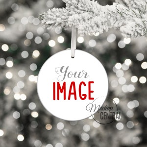 May include: White round Christmas ornament with the text "Your IMAGE" in red lettering. The ornament is hanging from a white string on a snowy branch with a blurred background of white lights.