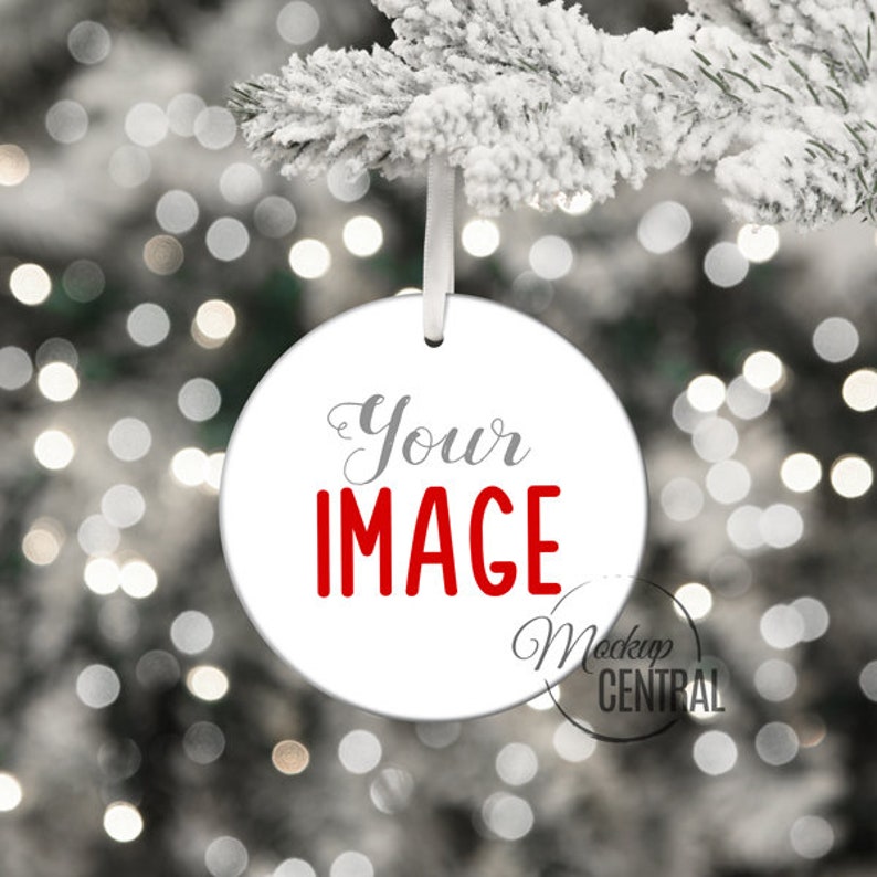 May include: White round Christmas ornament with the text "Your IMAGE" in red lettering. The ornament is hanging from a white string on a snowy branch with a blurred background of white lights.