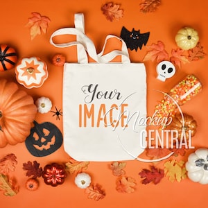 Może przedstawiać: Biała torba z napisem "Your IMAGE" w kolorze czarnym i pomarańczowym, otoczona dekoracjami na Halloween. Dekoracje obejmują dynie, liście, czaszkę i cukierki kukurydziane na pomarańczowym tle.