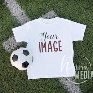 May include: White t-shirt with the text "Your Image" printed in brown on a green grass background with a white soccer ball.