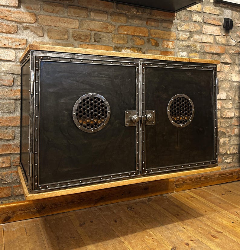 May include: A black metal cabinet with two doors and a wood top. The cabinet has two round metal vents with a honeycomb pattern. The cabinet is mounted on a wall.