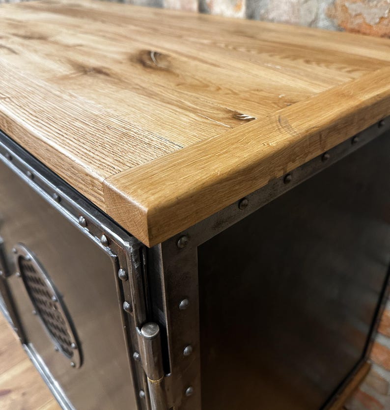 May include: A black metal cabinet with a wood top. The cabinet has a metal door with a hinge and a metal handle. The cabinet is decorated with metal rivets.