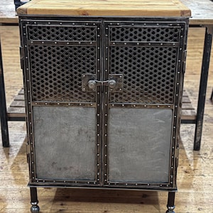 Könnte beinhalten: Ein Metallschrank mit zwei Türen, jede mit einem Metallgitter und einer massiven Metallplatte. Der Schrank hat eine Holzplatte und Metallbeine.