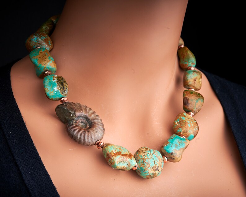 May include: A turquoise and brown stone necklace with a fossilised ammonite pendant. The necklace is made of large, irregular shaped stones with copper accents.