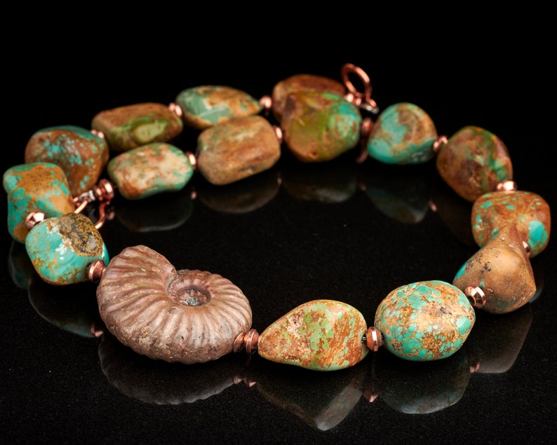 May include: A turquoise and copper necklace with a fossilised ammonite pendant. The necklace features irregularly shaped turquoise stones with brown and green marbling.