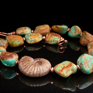May include: A turquoise and copper necklace with a large fossilized ammonite pendant. The necklace features a variety of turquoise stones with brown and green marbling.