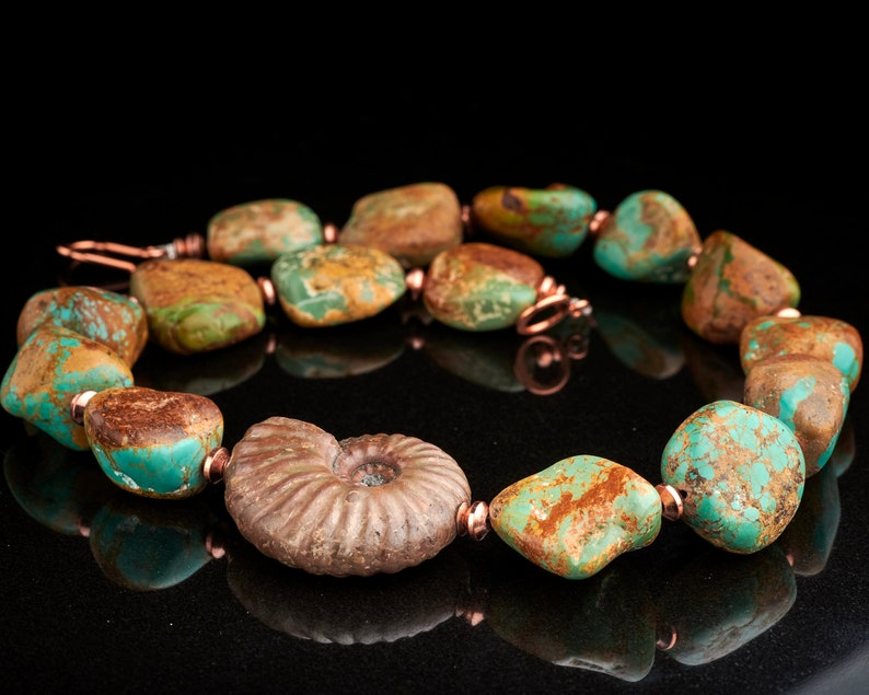 May include: A turquoise and copper necklace with a large fossilized ammonite pendant. The necklace features a variety of turquoise stones with brown and green marbling.