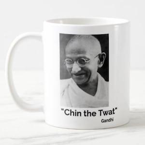 May include: White ceramic mug with a black and white portrait of a man in round glasses. The text "Chin the Twat" and the name "Gandhi" are printed below the image. The mug has a curved handle.