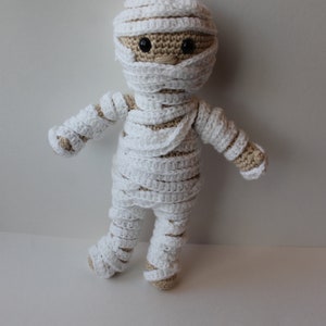 May include: A crocheted mummy doll with white bandages and brown yarn for the face and arms.