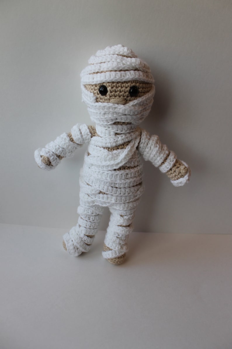 May include: A crocheted mummy doll with white bandages and brown yarn for the face and arms.