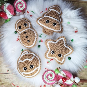 May include: Four crocheted gingerbread ornaments in the shape of a snowman, a star, a tree, and a bell. The ornaments are brown with white icing and black button eyes.