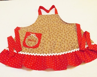 May include: A handmade apron featuring a tan fabric with a repeating brown floral pattern. The apron has a red polka dot skirt with white trim and a red pocket with the name "Melissa" embroidered on it. Red straps complete the design.