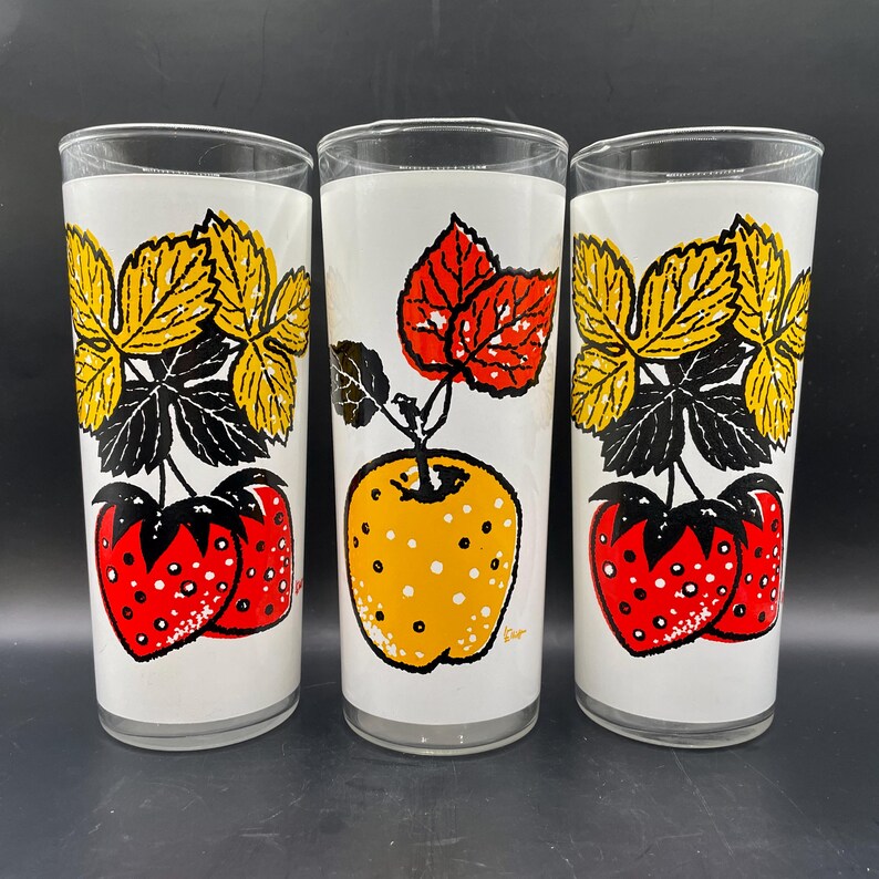 K&ouml;nnte beinhalten: Set aus drei klaren Glas-Trinkgl&auml;sern mit wei&szlig;em Hintergrund und einem bunten Design aus Erdbeeren, Bl&auml;ttern und einem Apfel. Das Design ist in Rot-, Gelb- und Schwarzt&ouml;nen gehalten.