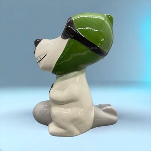 Ceramic Snoopy with green aviator hat and black goggles, riding a small gray plane.