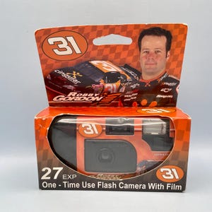 May include: Orange and black disposable camera in its original packaging. The packaging features a race car and a portrait of Robby Gordon. The camera has the number 31 and the text "One-Time Use Flash Camera With Film".