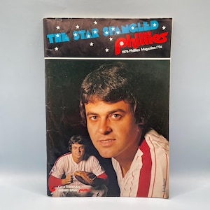 Puede incluir: Portada de la revista Phillies de 1976 con un retrato de un jugador de béisbol. El título de la revista, "The Star Spangled Phillies", está en azul y rojo. La portada también incluye el texto "1976 Phillies Magazine/75¢."
