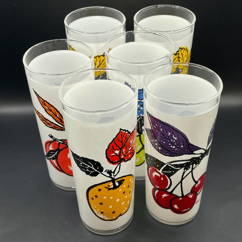 Six  glass tumblers with colorful fruit illustrations. The glasses have a white background with black outlines and feature cherries, grapes, apples, and leaves in shades of red, orange, yellow, green, purple, and black.