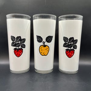 K&ouml;nnte beinhalten: Drei wei&szlig;e Glasbecher mit schwarzen und roten Fruchtillustrationen. Die Becher zeigen eine Erdbeere, einen Apfel und eine Erdbeere.