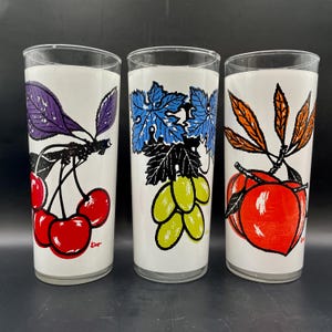 K&ouml;nnte beinhalten: Drei klare Glasbecher mit wei&szlig;em Hintergrund und bunten Fruchtillustrationen. Der erste Becher zeigt lila und schwarze Kirschen, der zweite zeigt eine blaue und gr&uuml;ne Weintraube und der dritte zeigt orange und rote Pfirsiche.