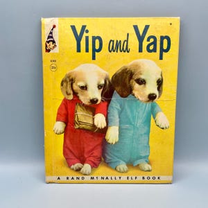 May include: Vintage children's book titled "Yip and Yap" with a yellow cover. The cover features two puppies wearing red and blue jumpsuits. The book is a Rand McNally Elf Book.