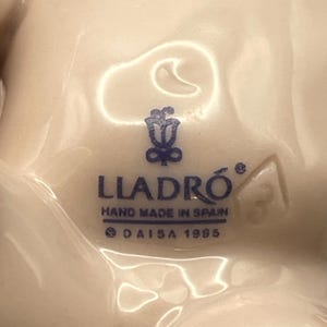 May include: Close-up of a white porcelain figurine base with the blue text "LLADR&Oacute; HAND MADE IN SPAIN &copy; DAISA 1985". The logo features a floral design. A number "3" is visible.