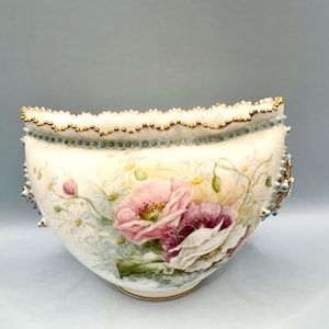 May include: A white porcelain bowl with a scalloped rim, adorned with gold trim and turquoise accents. The bowl features hand-painted pink and white poppies, daisies, and green foliage, creating a floral design. The bowl has a gold base.